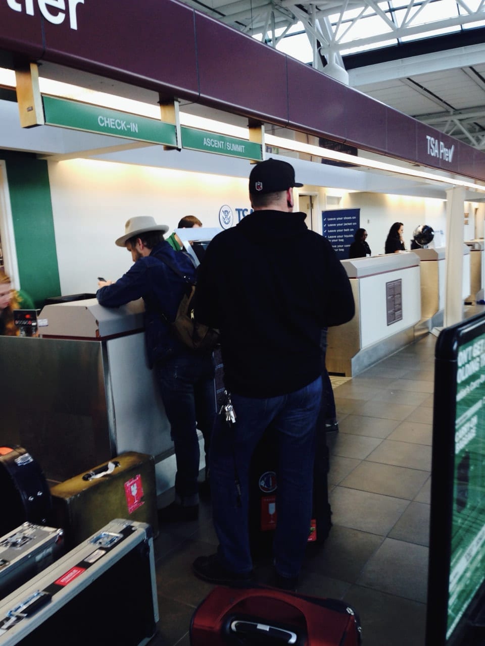 Two unidentified travelers at a TSA PreCheck counter with instrument and road cases around them.