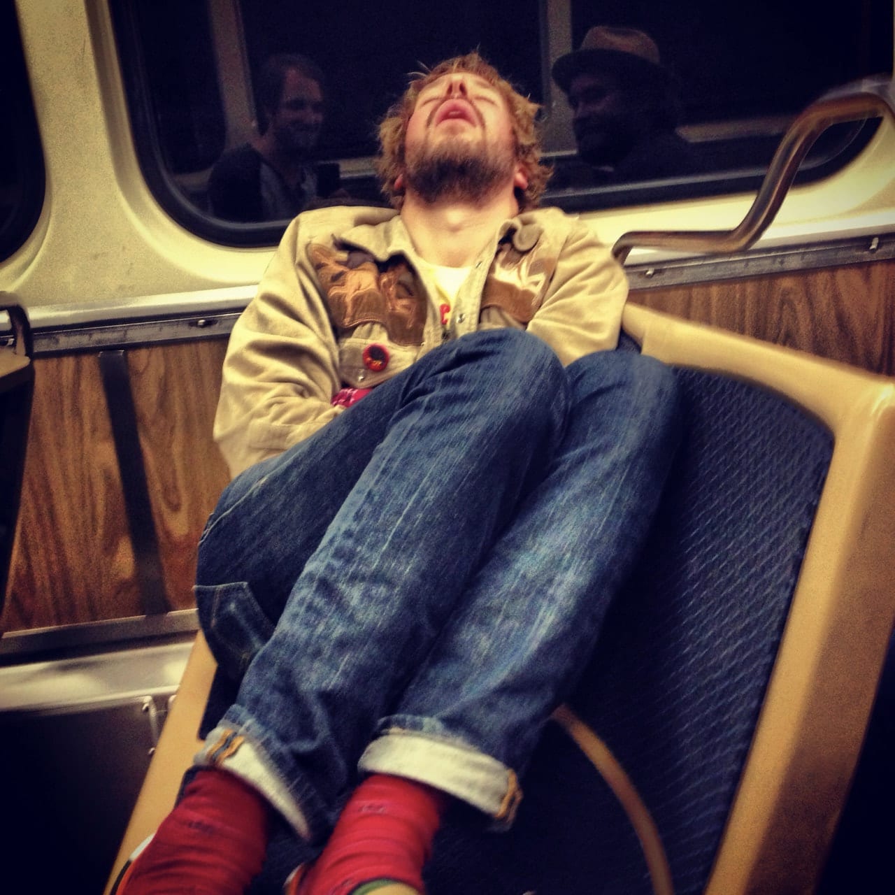 Unidentified band member asleep upright in a molded seat aboard a bus, train, or other transit vehicle.