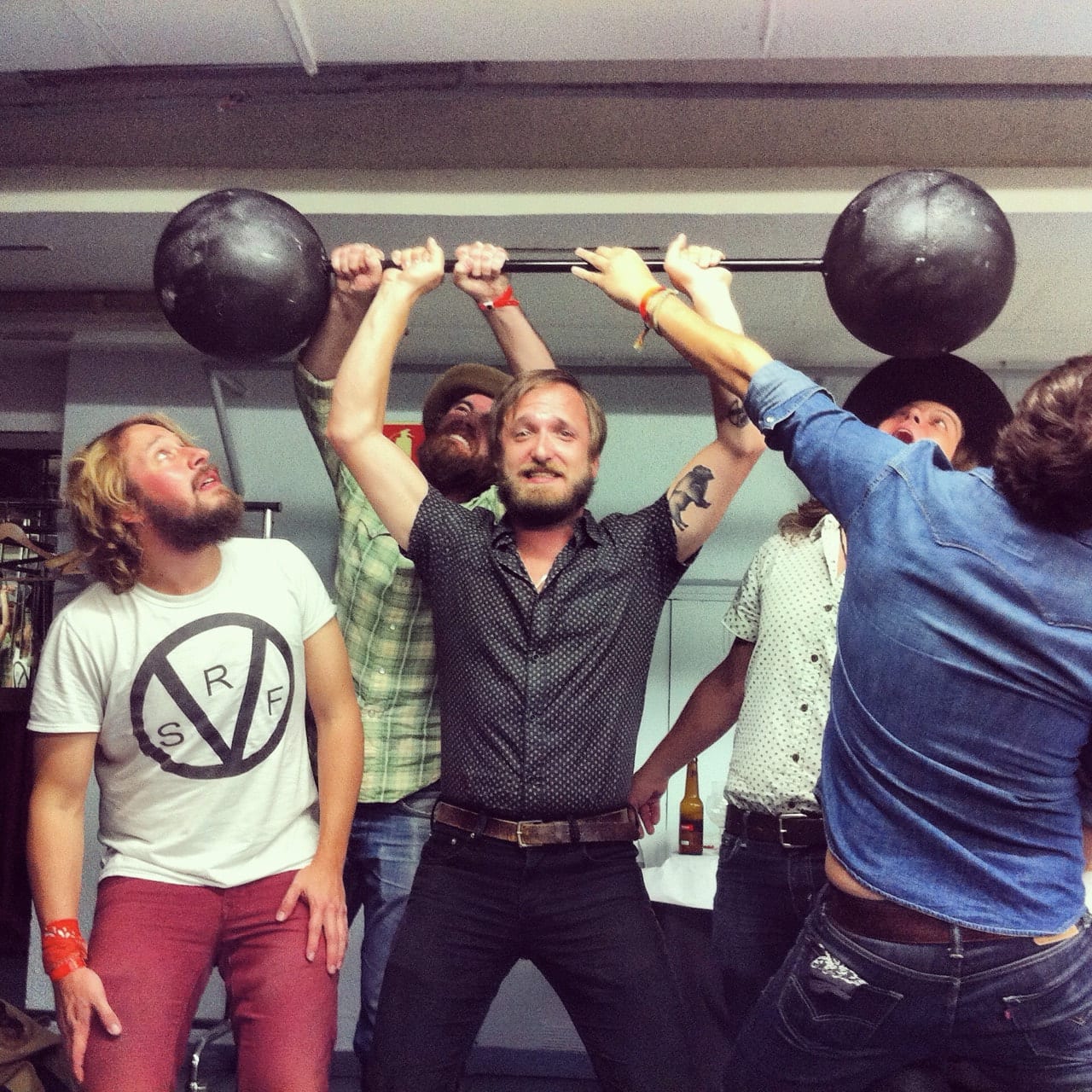 Five unidentified Wild Feathers members or associates gathered around a barbell backstage.