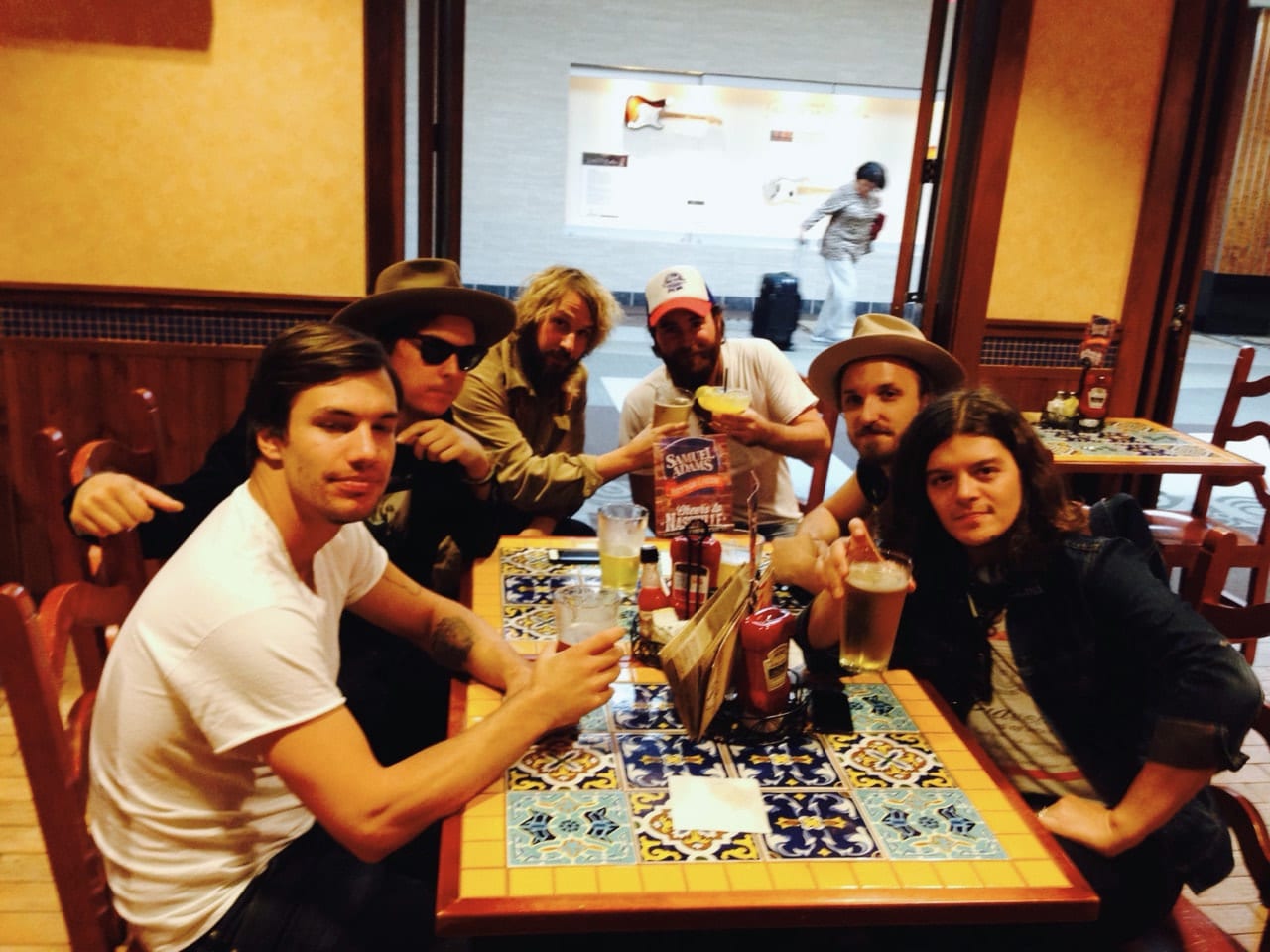 Six unidentified members or associates of The Wild Feathers gathered around a tiled restaurant table.