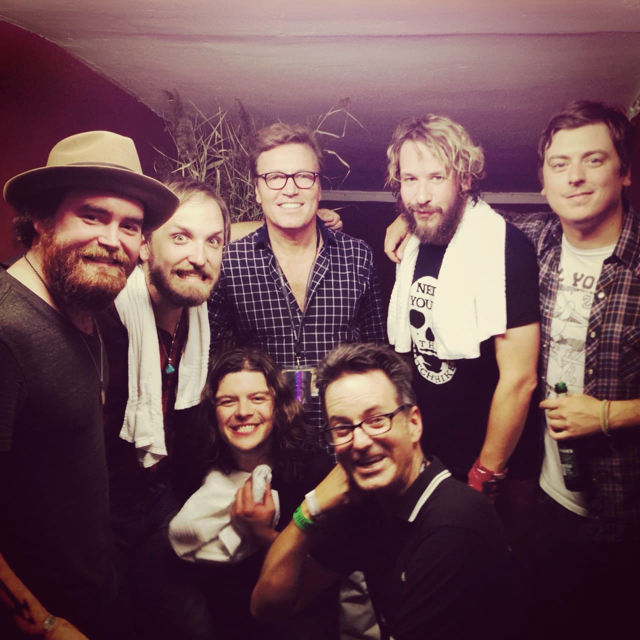 Five unidentified Wild Feathers members and two unidentified guests smiling together backstage after a performance.