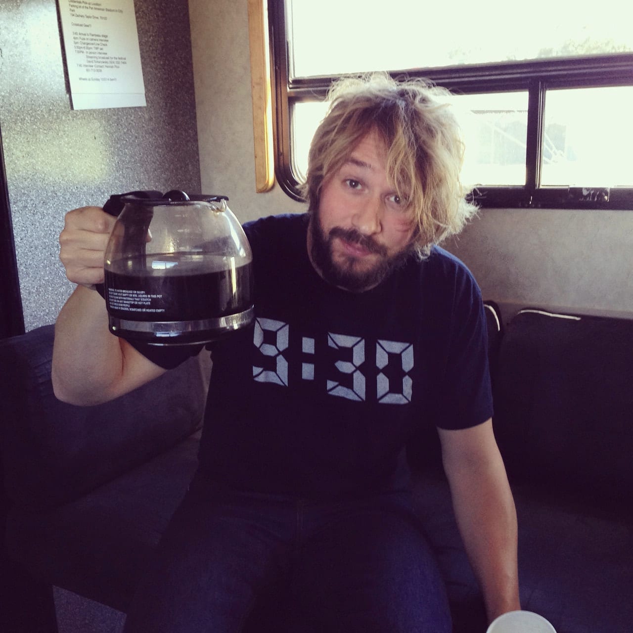 Unidentified Wild Feathers member seated on a tour bus and holding up a glass coffee pot.