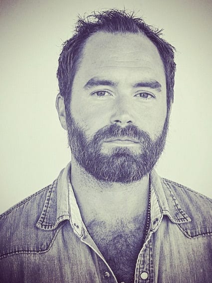 Stylized blue-gray head-and-shoulders portrait of an unidentified bearded member of The Wild Feathers.
