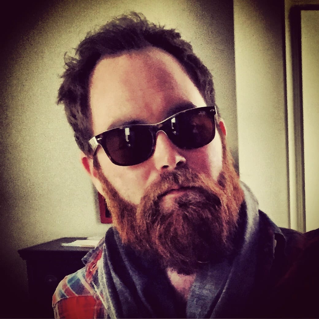 Close self-portrait of an unidentified bearded member of The Wild Feathers wearing dark sunglasses.