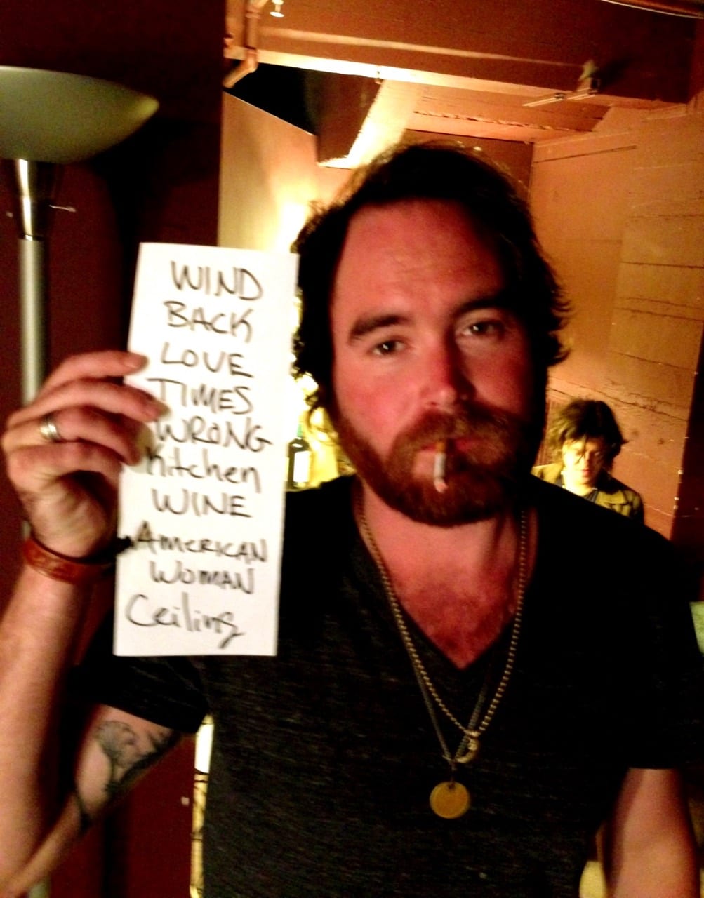 Unidentified band member holding a handwritten set list while another person stands in the background.