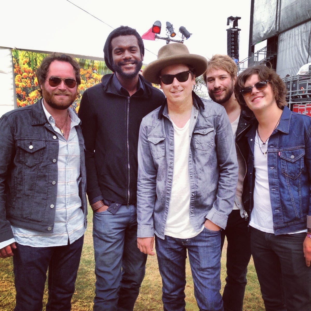 Four unidentified Wild Feathers members standing with an unidentified guest beside an outdoor festival stage.