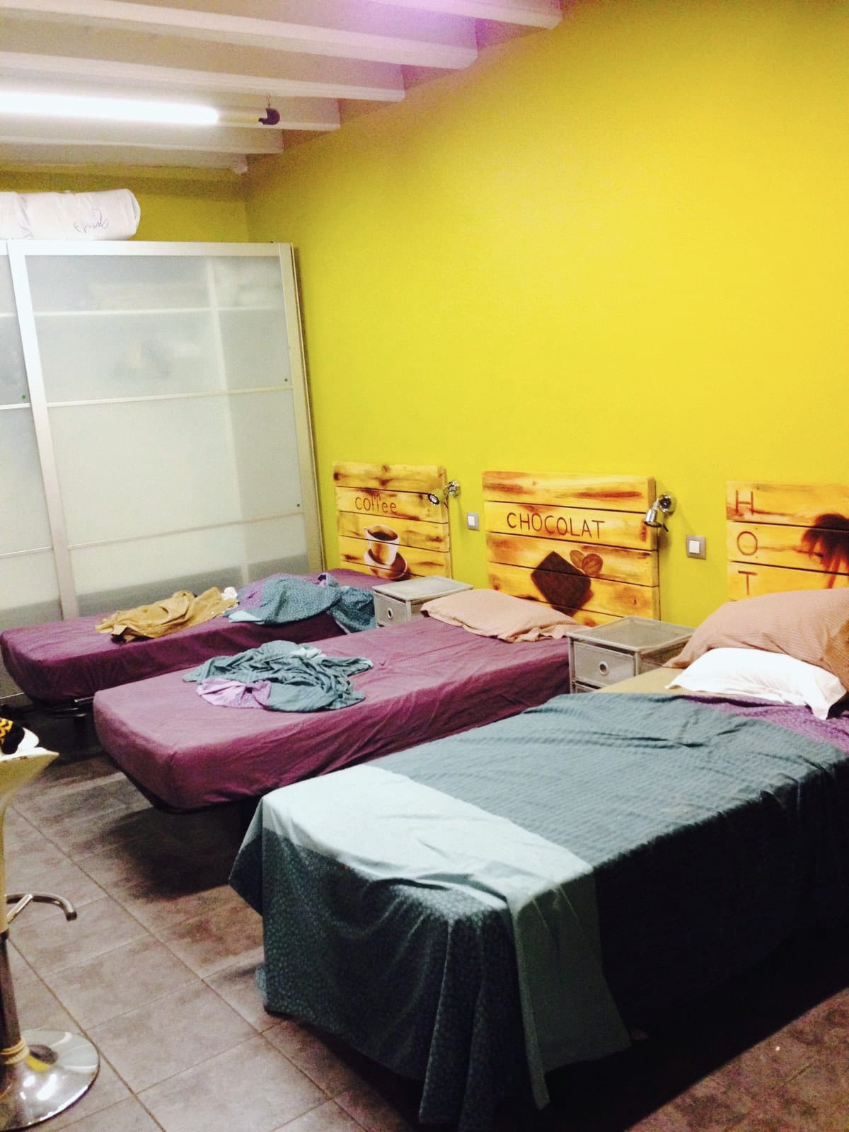 Two narrow beds with bright bedding sit inside a small yellow-walled room.