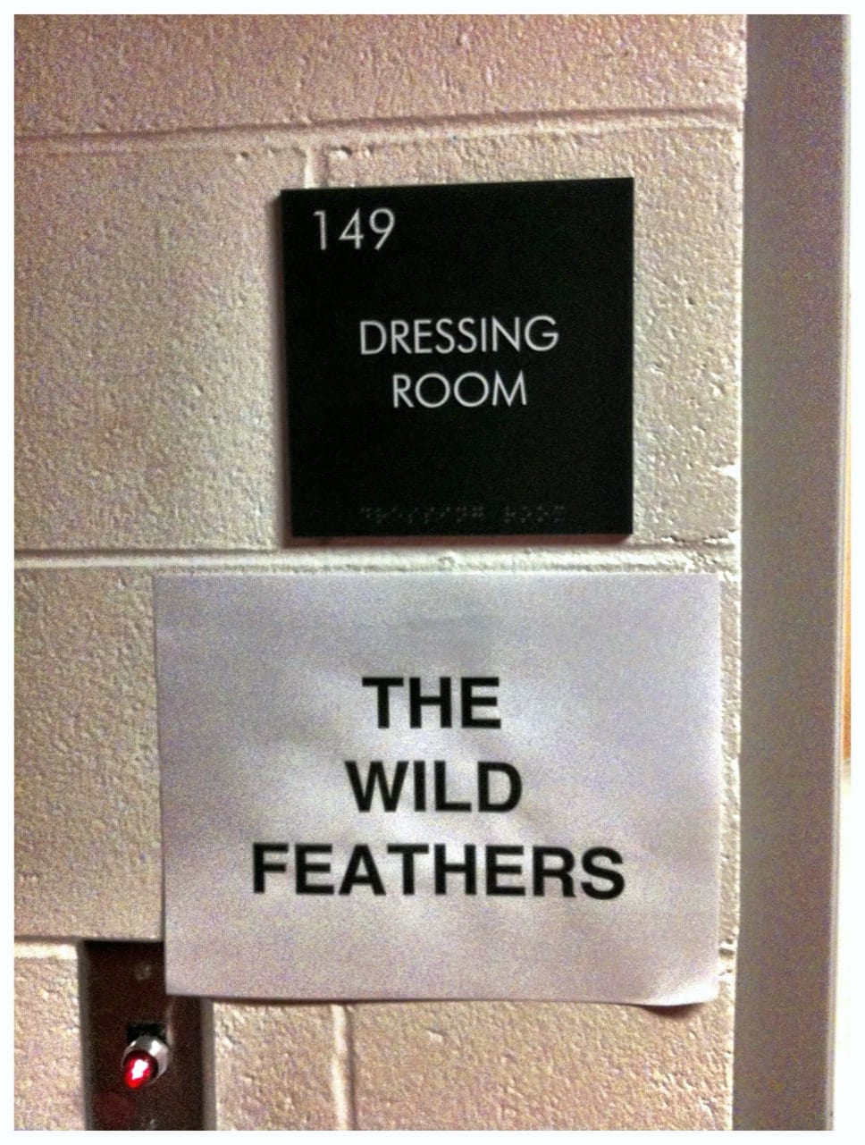 Venue wall sign reading Dressing Room 149 above a paper sign labeled The Wild Feathers.