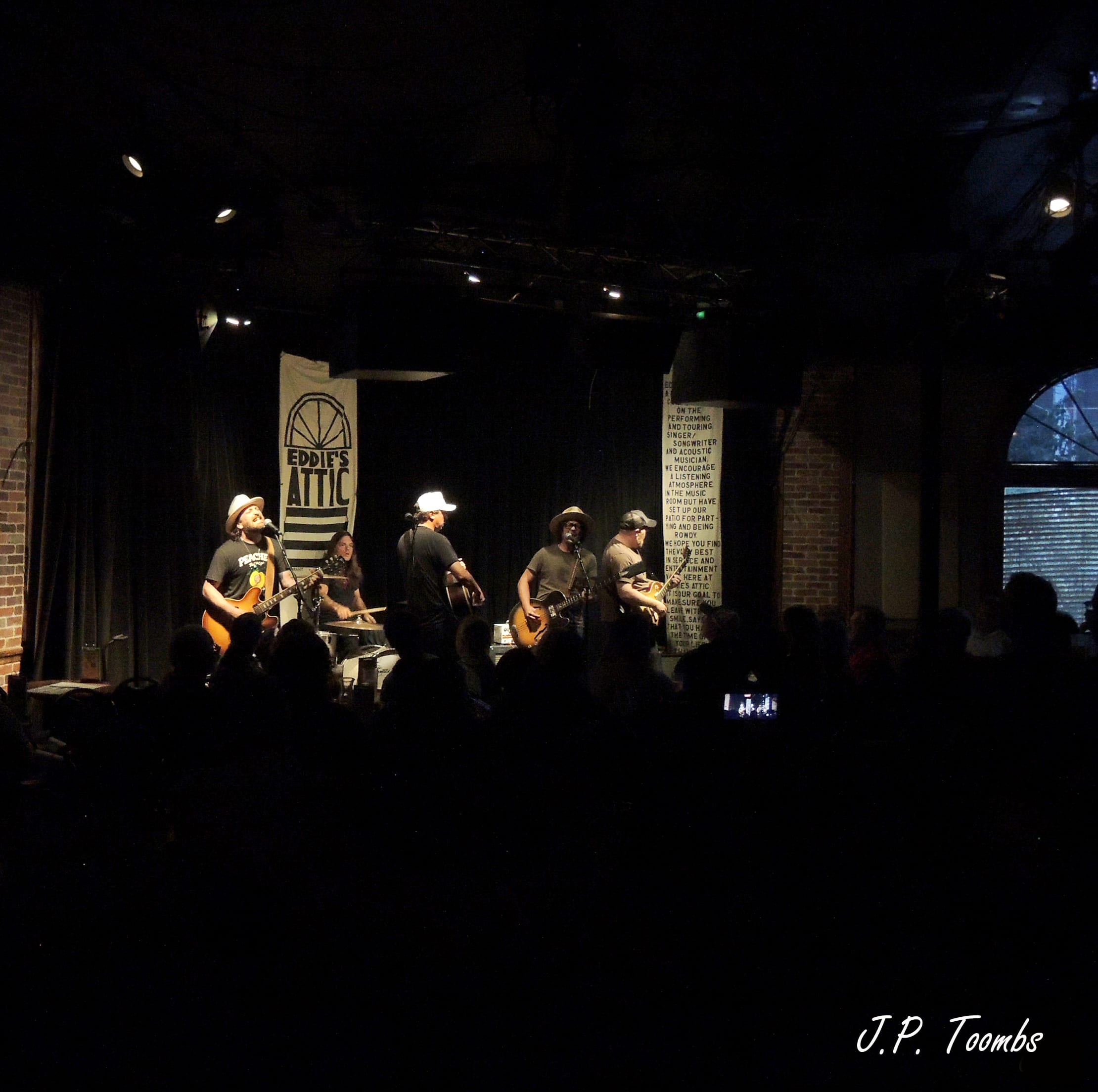 The Wild Feathers perform beneath the Eddie's Attic sign while a tightly packed seated audience fills the dark room.