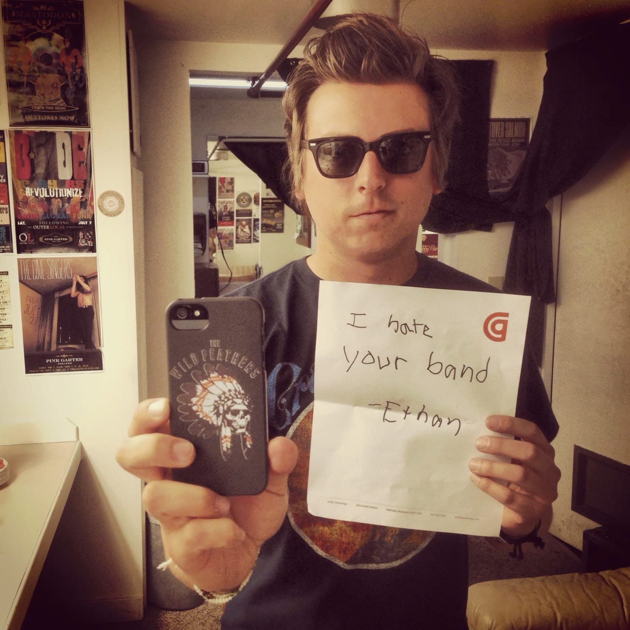 Unidentified band member making a mirror self-portrait while holding a handwritten note reading I hate your band, signed Ethan.