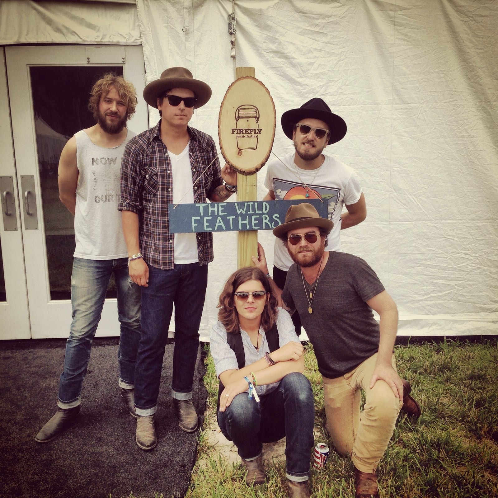 Members of The Wild Feathers and companions posing in front of a festival tent in Dover.