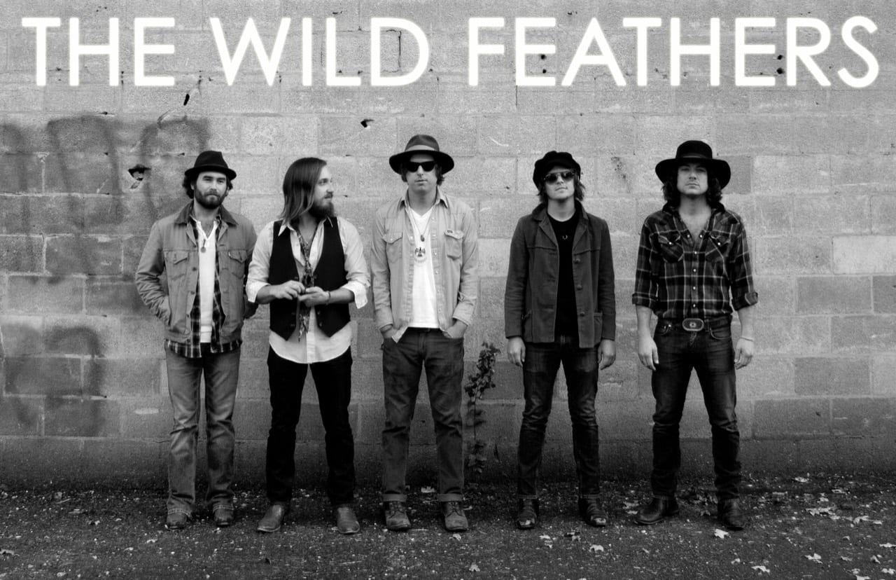Black-and-white promotional portrait of five Wild Feathers members standing against a concrete block wall.