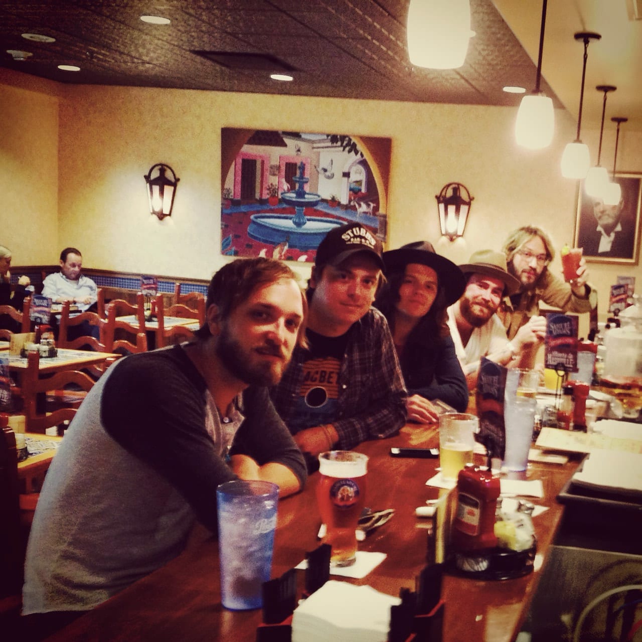Five unidentified Wild Feathers members gathered at a restaurant table with drinks after or between tour travel.