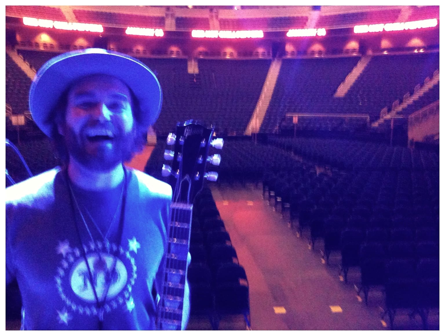 The founding guitarist smiling with a guitar onstage in an empty theater after soundcheck.