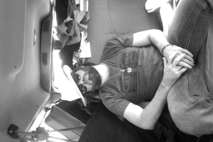 A sideways black-and-white photograph of the founding guitarist sleeping across seats inside a van.