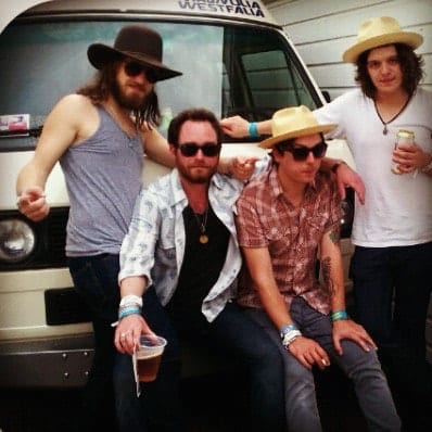 Four unidentified Wild Feathers members gathered beside a white vehicle during SXSW, wearing hats and festival-style wristbands.