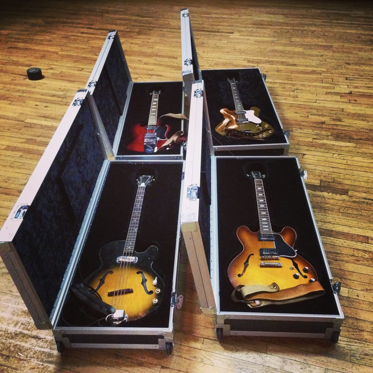 Four electric and hollow-body guitars resting in open road cases on a wooden floor.