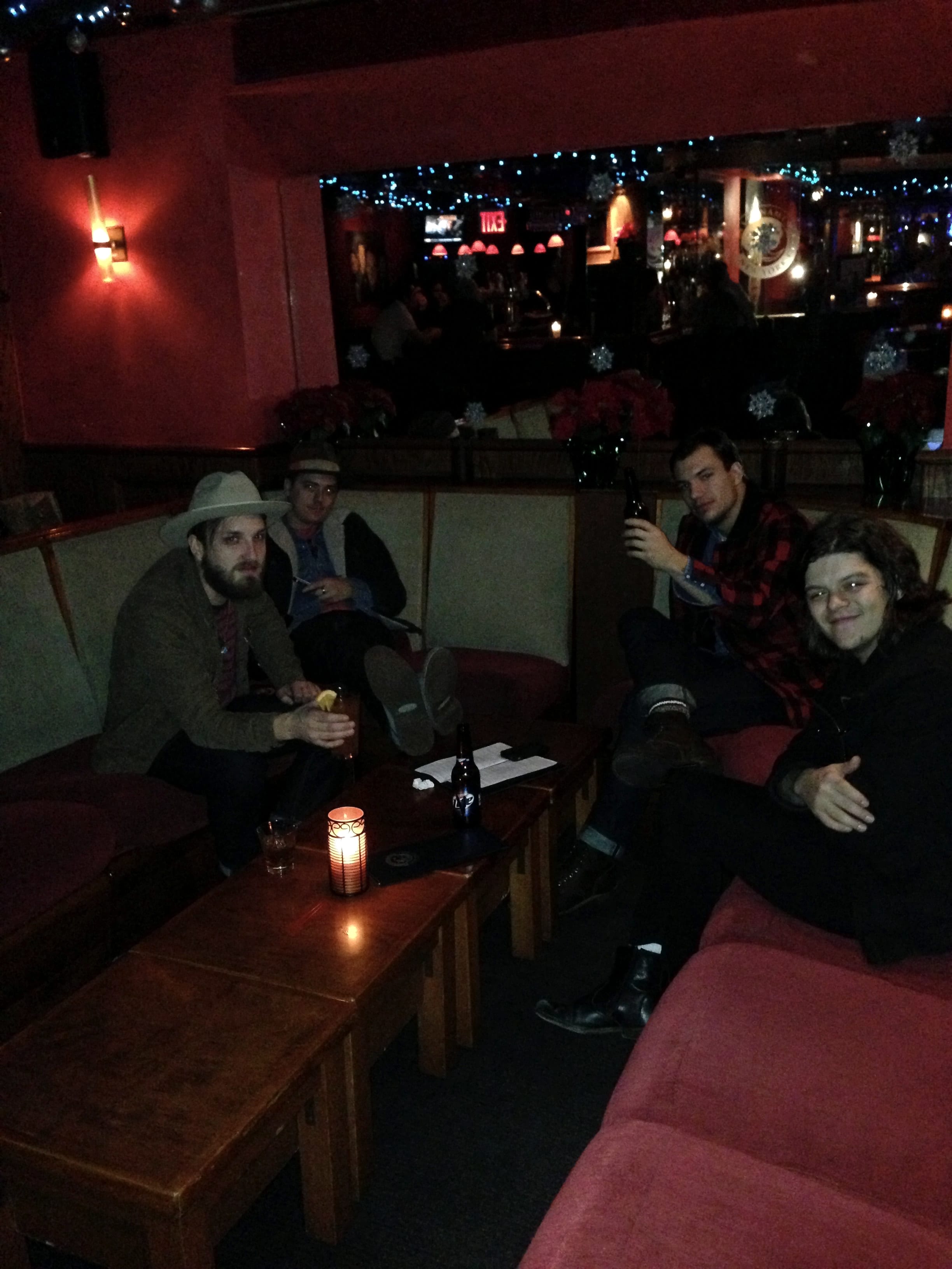 Four unidentified members of The Wild Feathers seated around small tables in a dim red lounge decorated with blue lights and snowflakes.