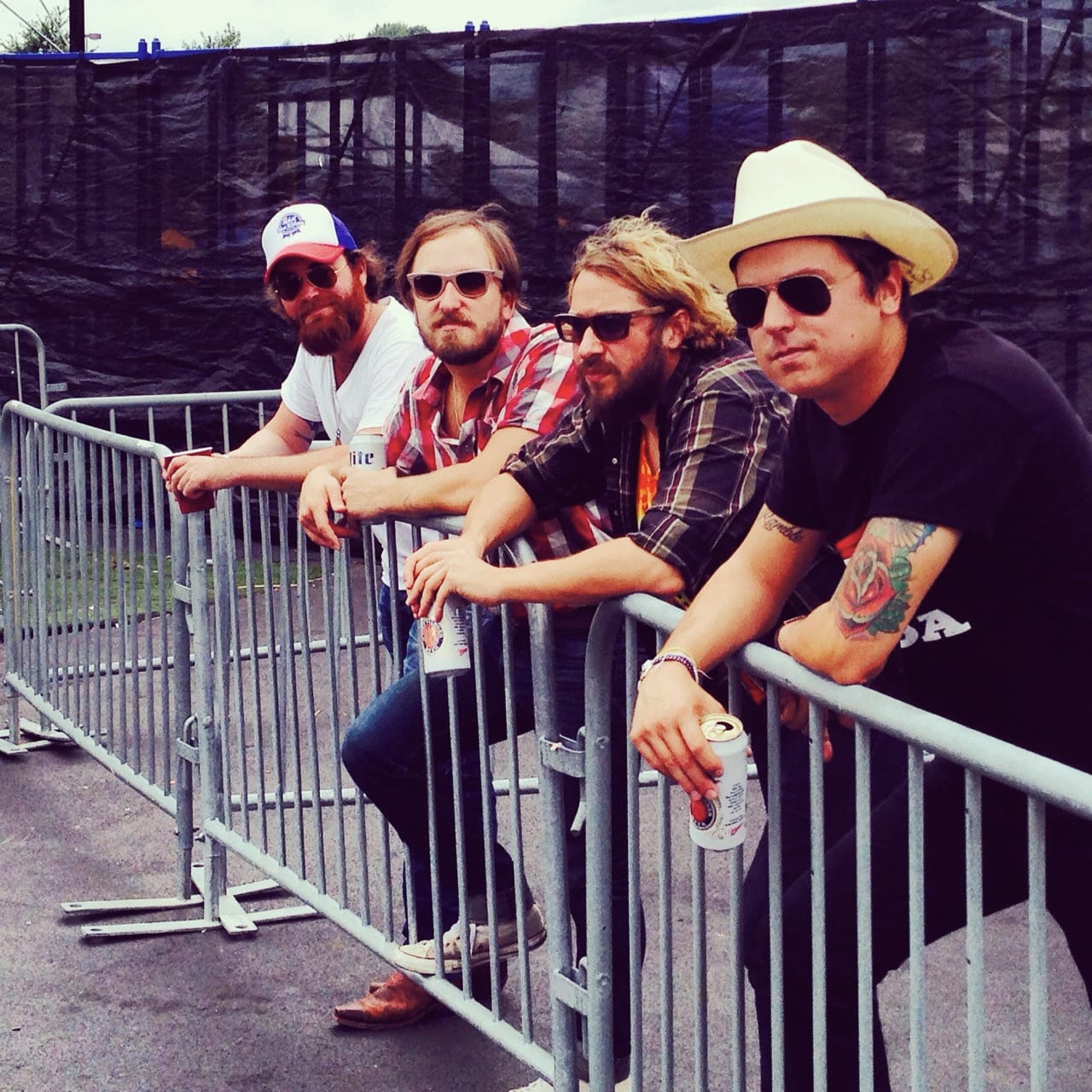 Four unidentified Wild Feathers members leaning on a crowd-control barrier beside an outdoor stage.