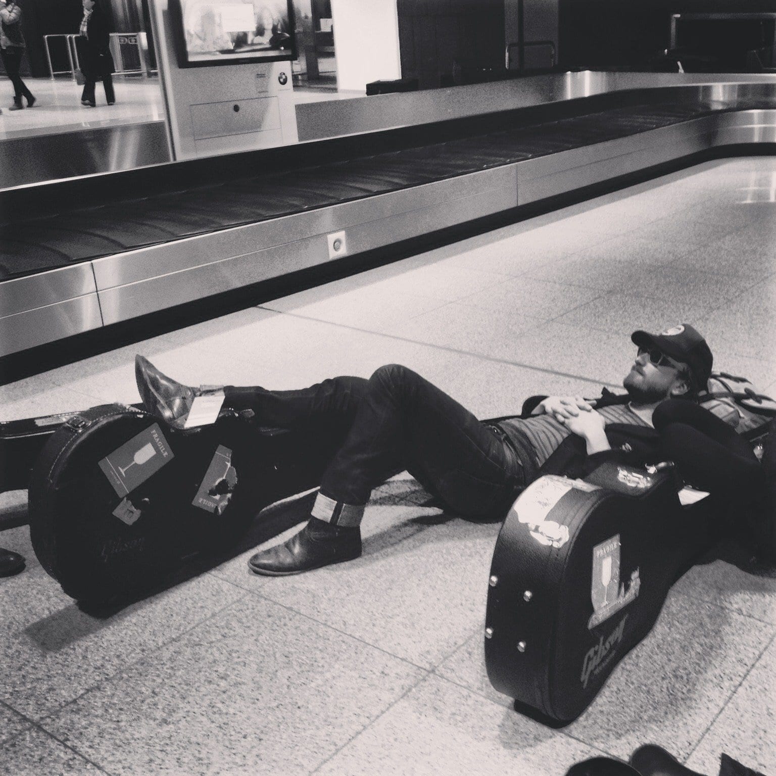 A traveler sleeping across airport seats with guitar cases beside him in Hamburg.