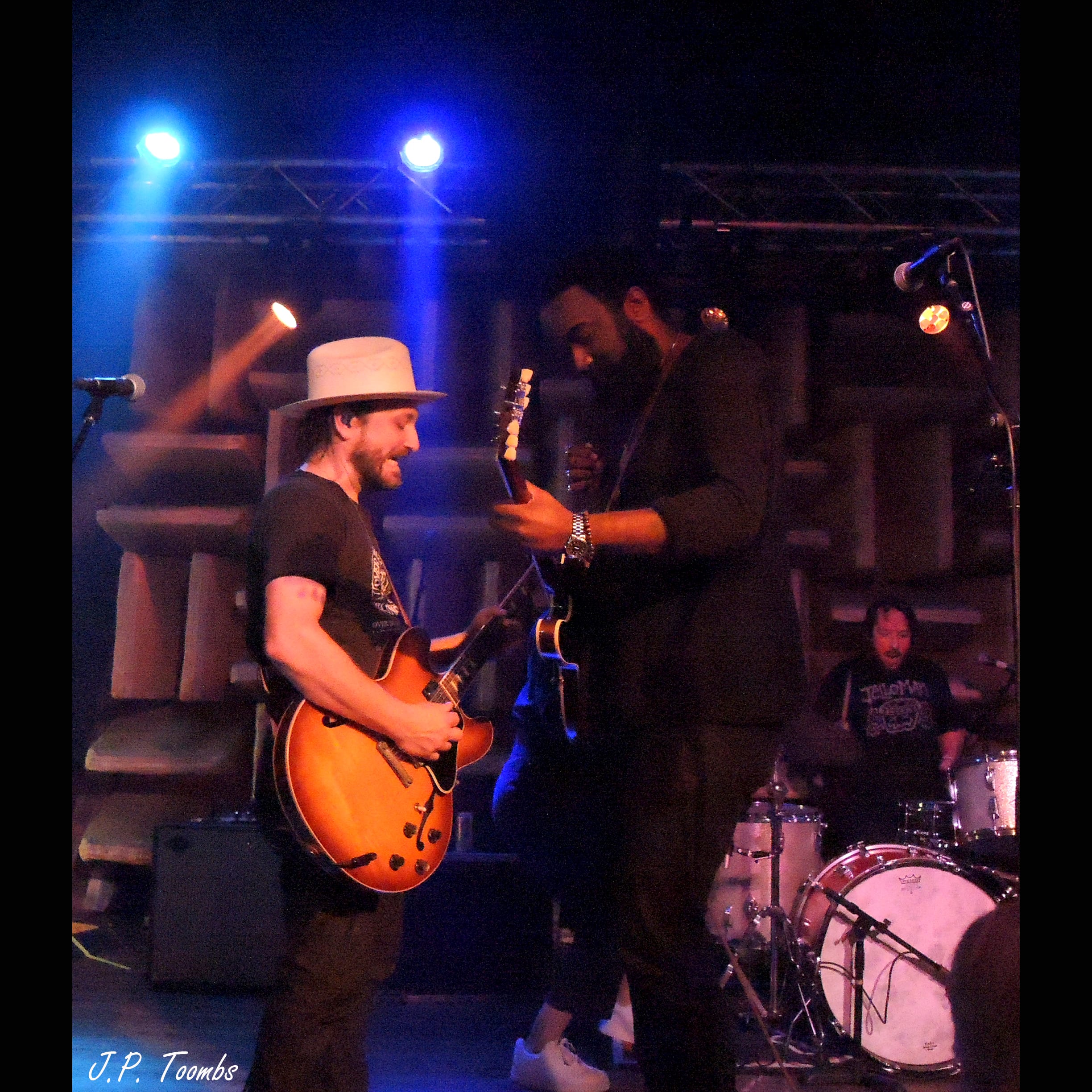 Two guitarists face one another at center stage while a drummer plays behind them during the HI-FI Indy encore.