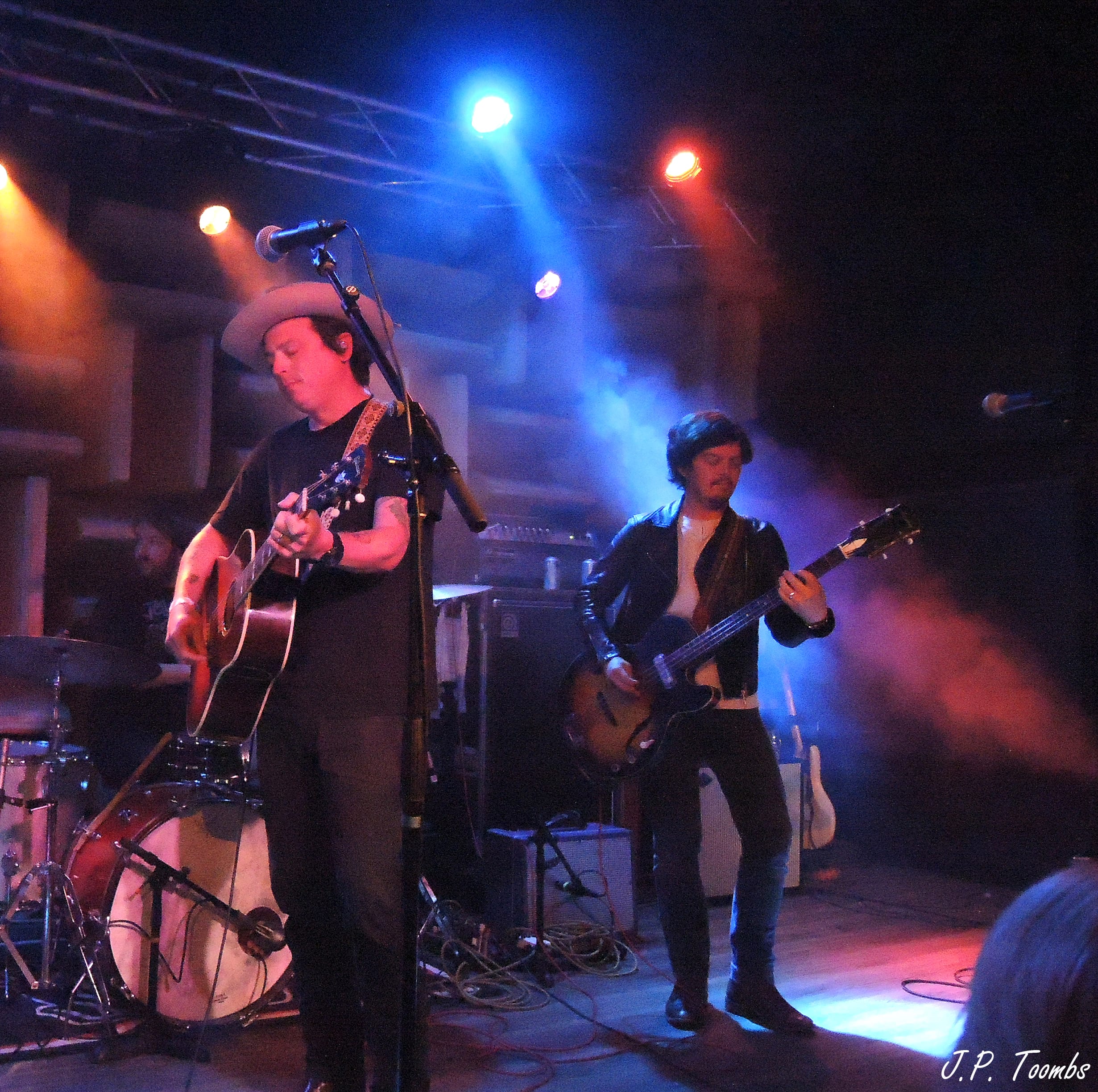 Members of The Wild Feathers perform with acoustic and electric guitars under blue and amber lights at HI-FI Indy.