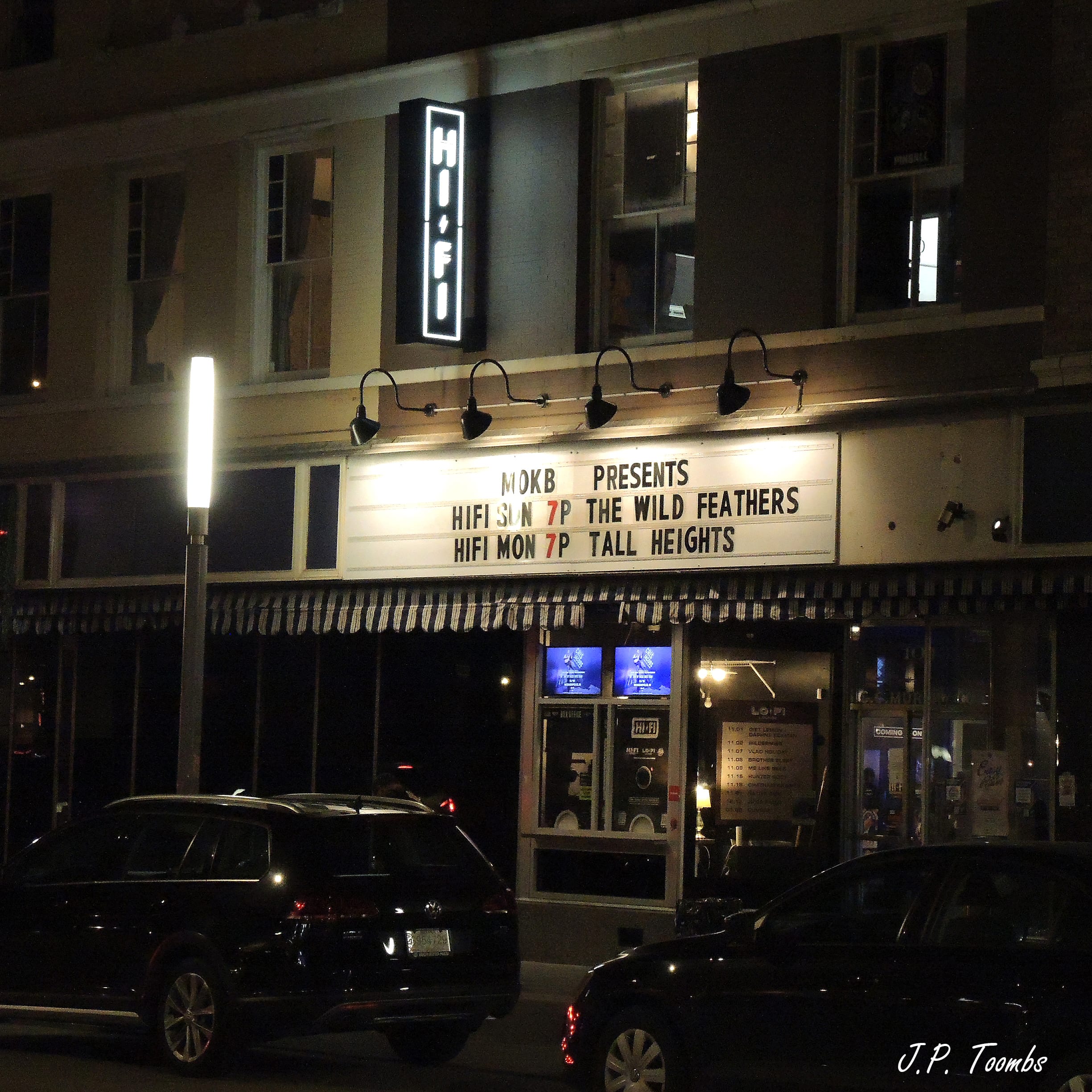 The illuminated HI-FI Indy entrance and marquee list The Wild Feathers above Tall Heights on a dark Indianapolis street.