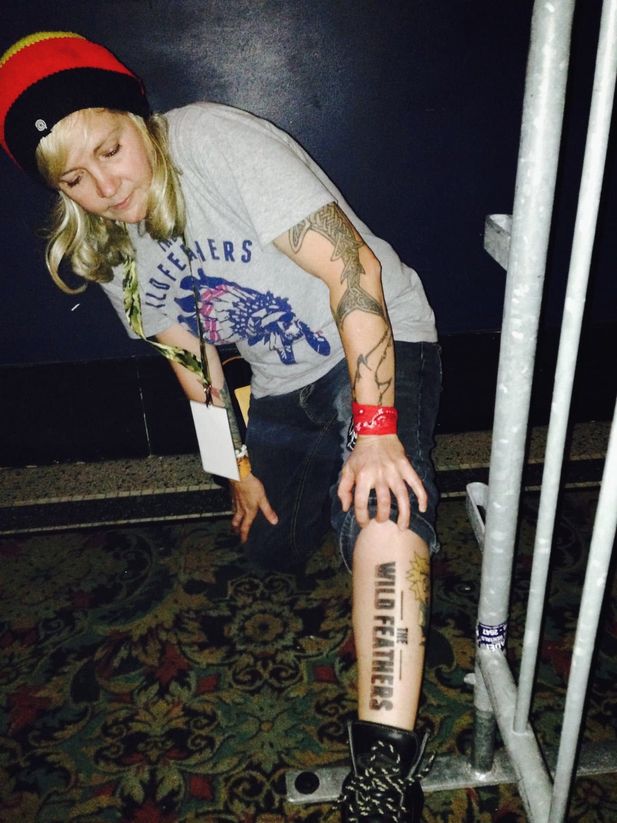 A person in a Wild Feathers shirt and cap shows a Wild Feathers tattoo on their lower leg backstage in Indianapolis.