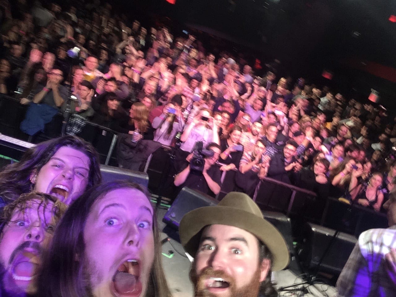 Four unidentified Wild Feathers members taking a selfie from the stage with a large applauding audience behind them.