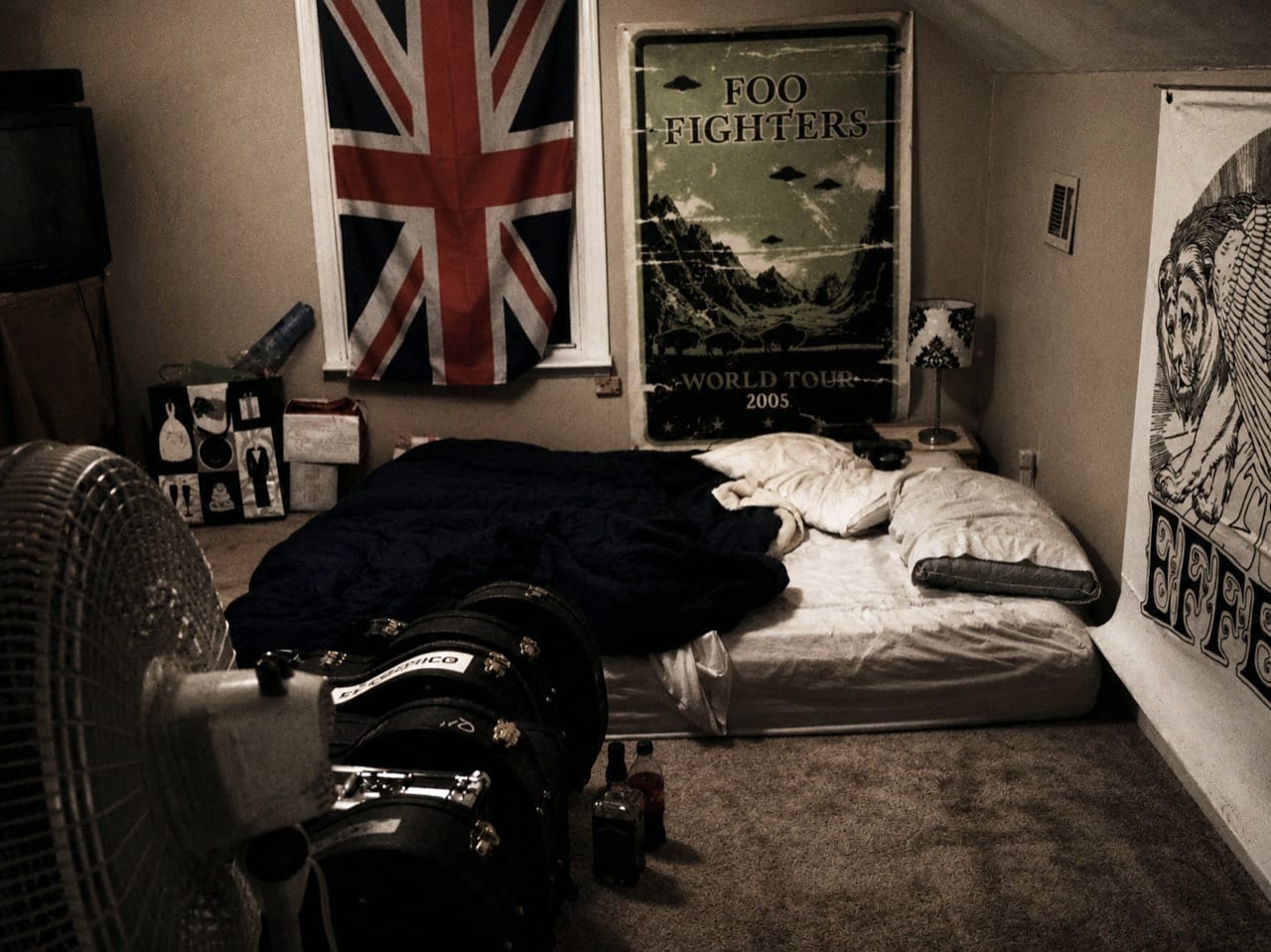A borrowed bedroom in Nashville with a blow-up mattress on the floor, instrument cases, a Union Jack, and music posters.