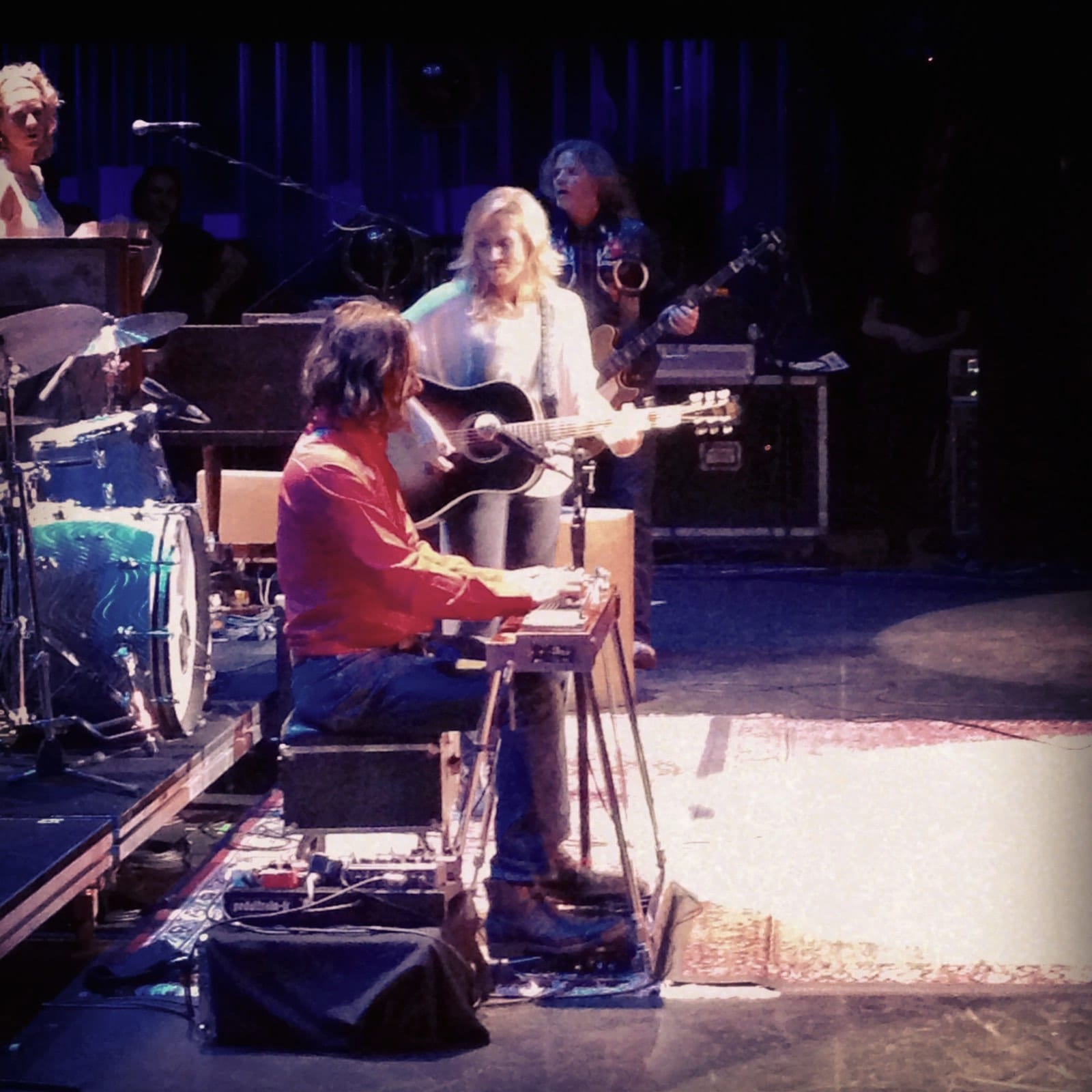A side-stage view of musicians, keyboards, drums, and amplifiers during the Kingston tour stop.