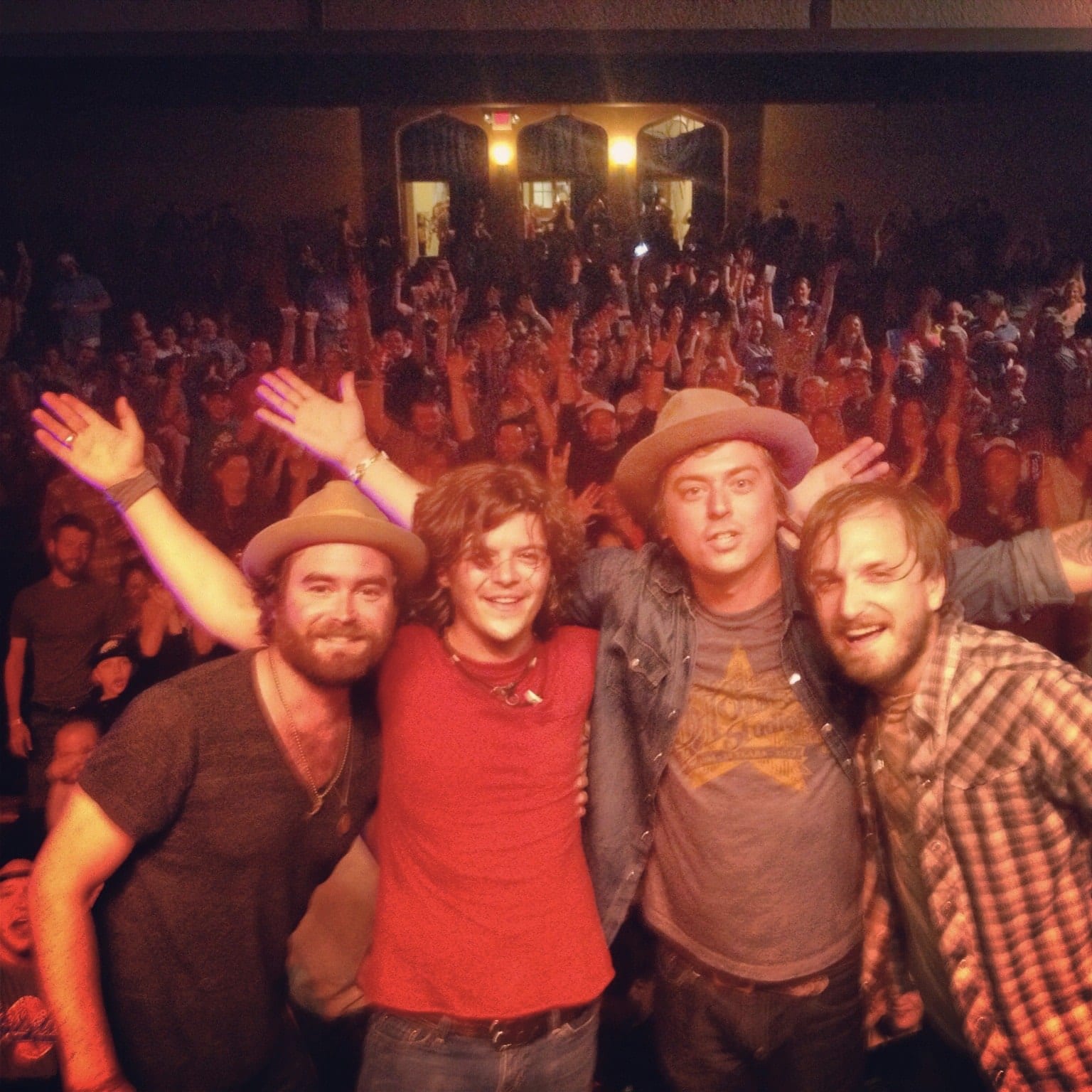 Four members of The Wild Feathers posing at the front of the stage with the Laramie audience behind them.