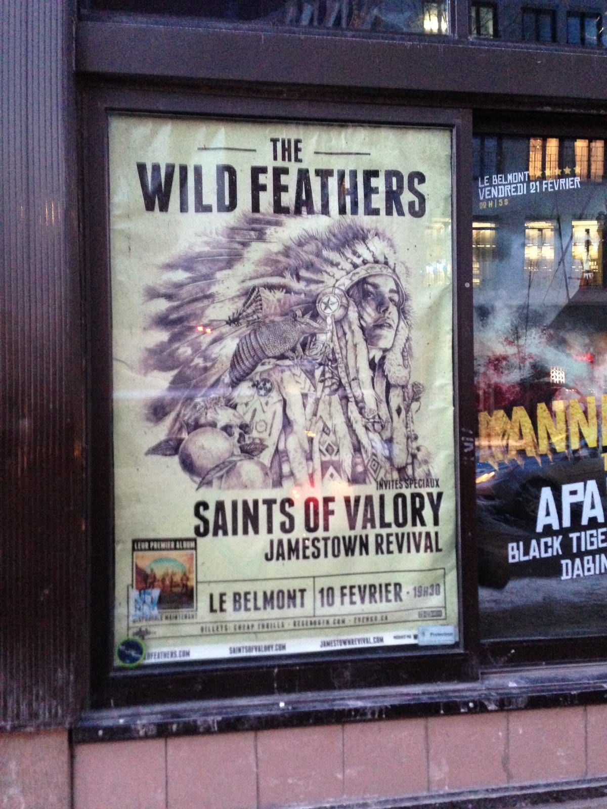 A Montreal venue window displaying a Wild Feathers poster with Saints of Valory and Jamestown Revival.