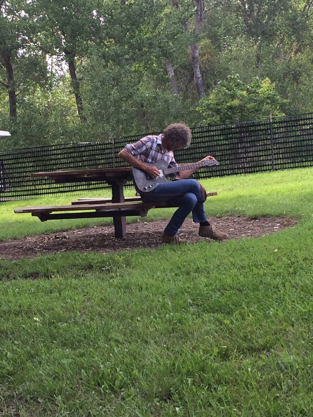 Audley Freed sitting alone at a park bench and playing acoustic guitar before soundcheck in Littleton, Colorado.