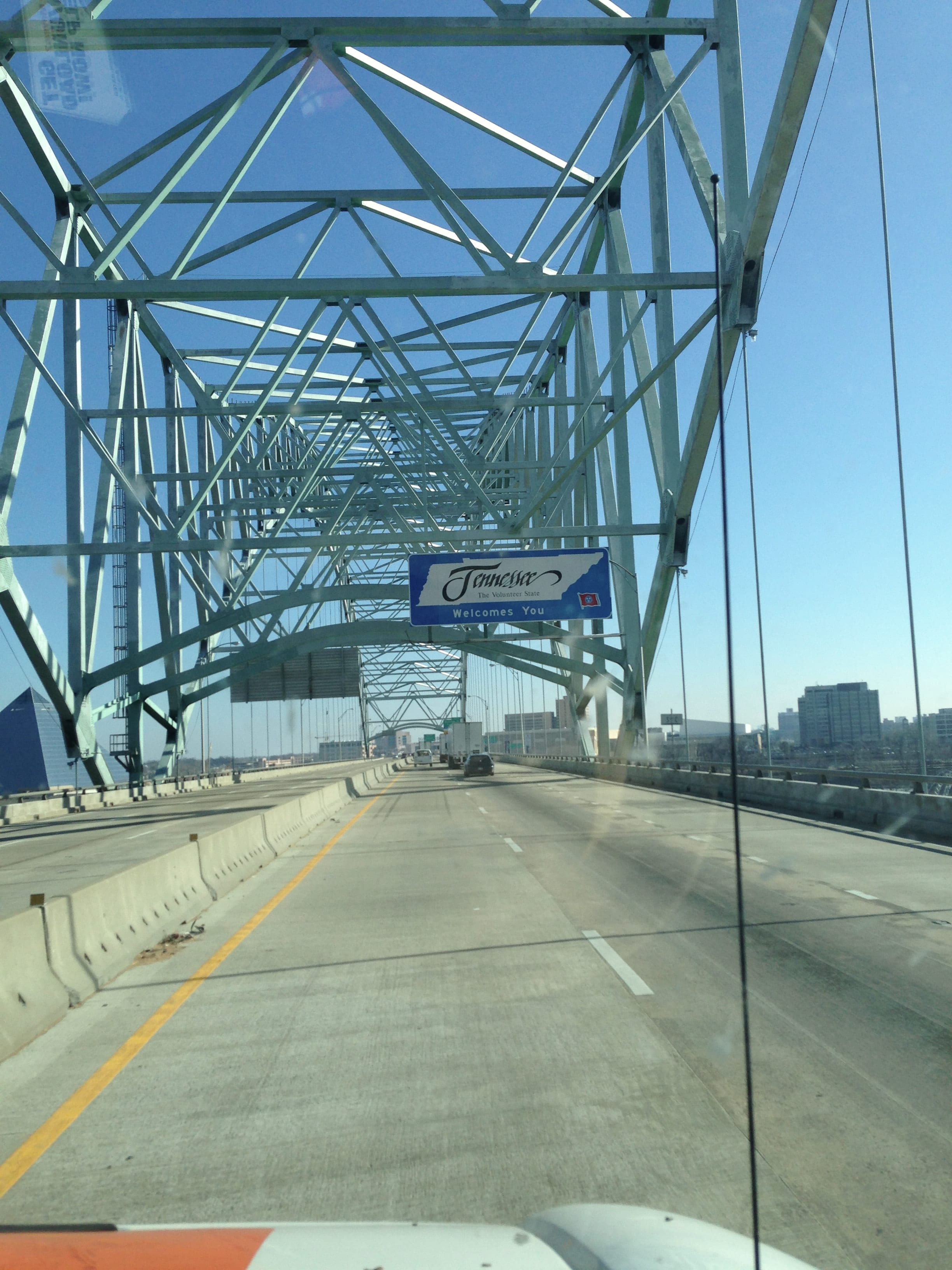 A view through a vehicle windshield while crossing a bridge beside a Welcome to Memphis sign.
