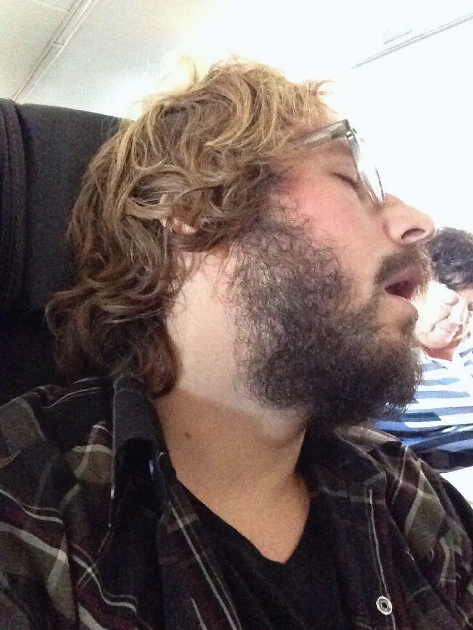 A bearded passenger is photographed in profile inside a vehicle.