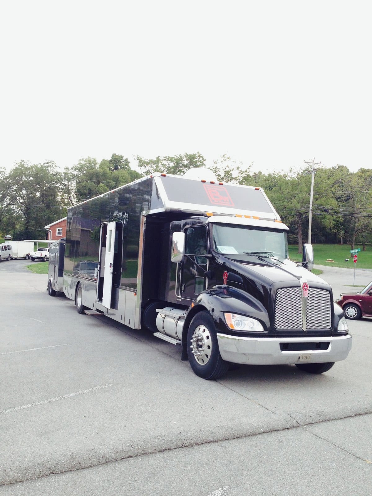 A black tour bus with a white trailer is parked beside a road in Nashville.