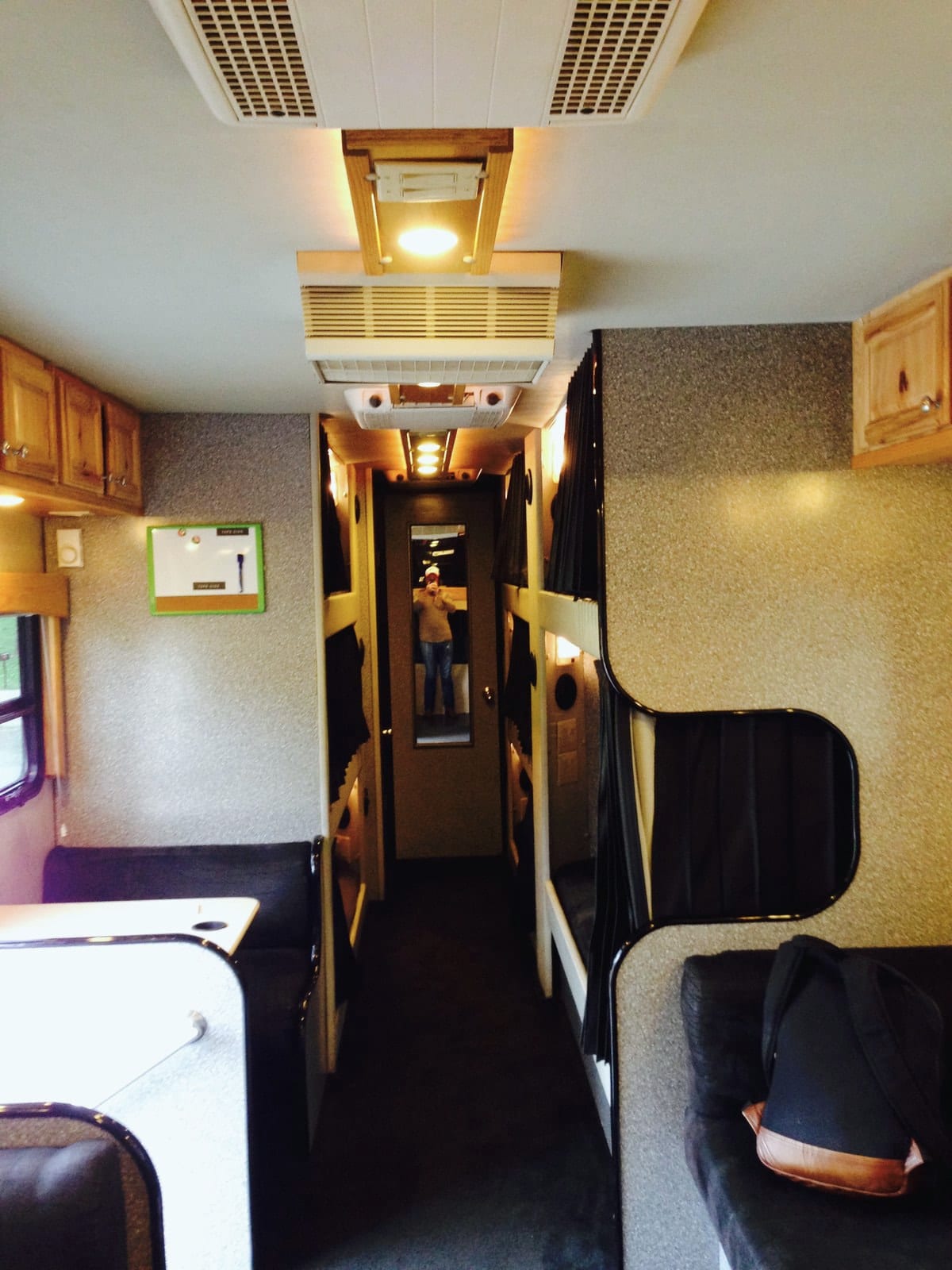 The empty central aisle and bunks of a tour bus are seen from the front lounge.