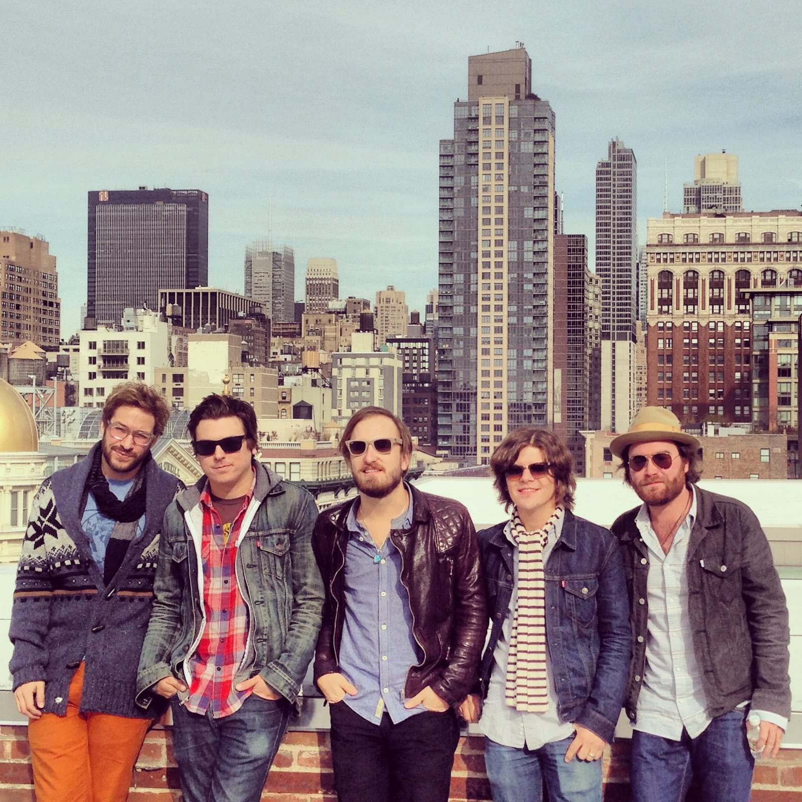 Five members of The Wild Feathers posing on a rooftop with the New York skyline behind them.