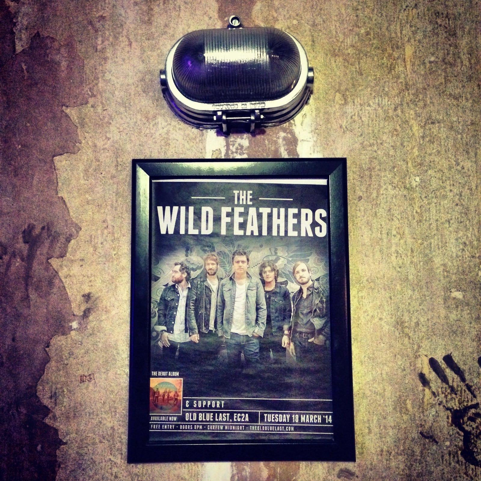 A framed Wild Feathers concert poster mounted inside The Old Blue Last in London.