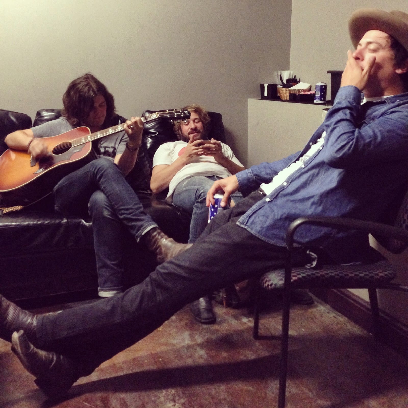 Three members of The Wild Feathers sitting with guitars and drinks in a dressing room in St. Louis.