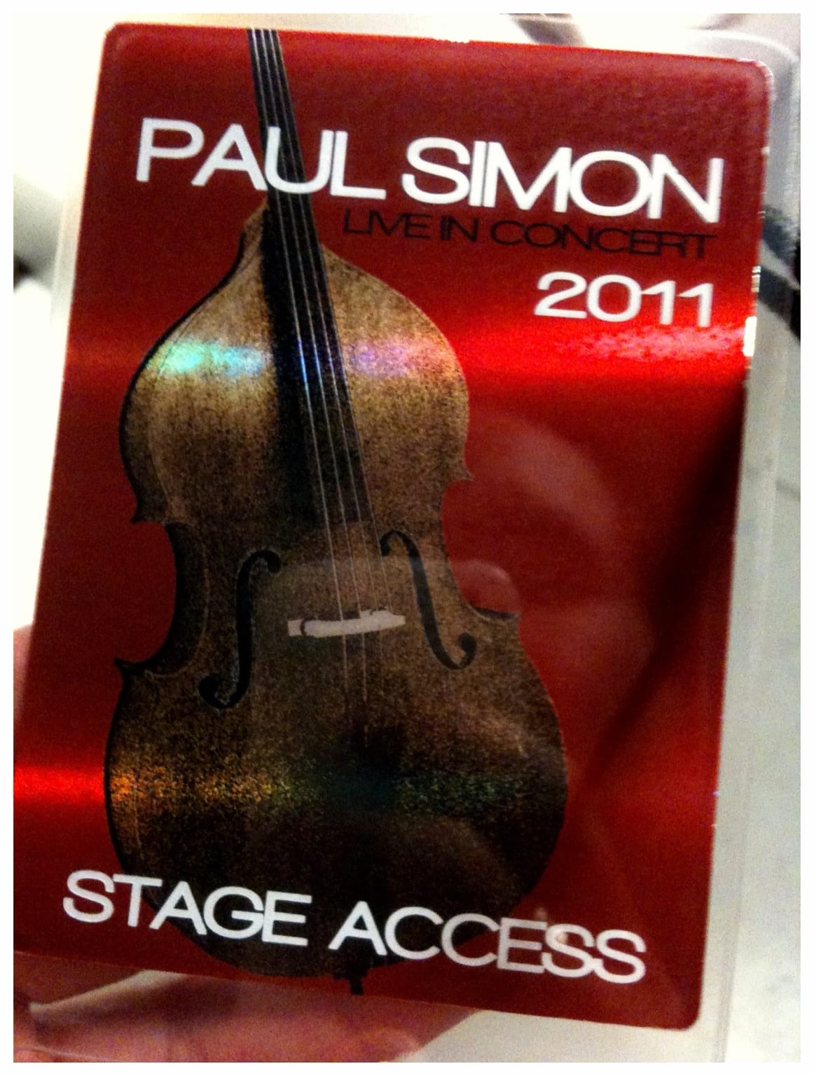 A red Paul Simon Live in Concert 2011 stage-access pass with an upright bass graphic.