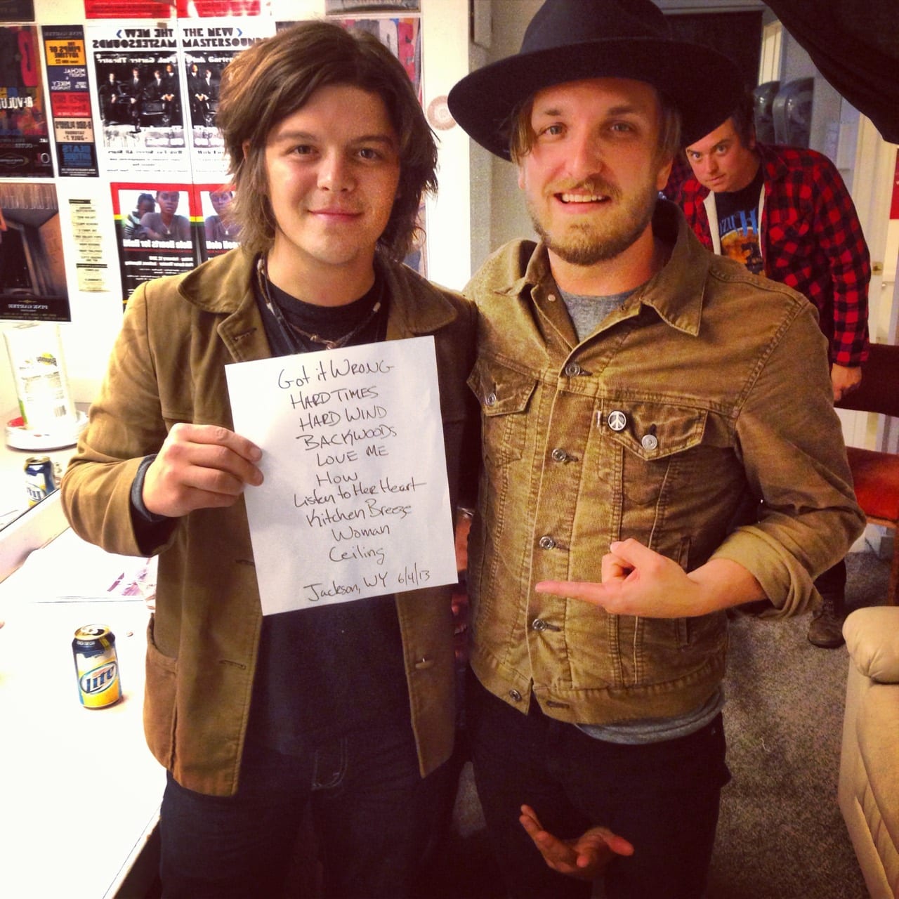 Two unidentified band members holding a handwritten Wild Feathers set list dated Jackson, Wyoming, June 4, 2013, with a third person behind them.
