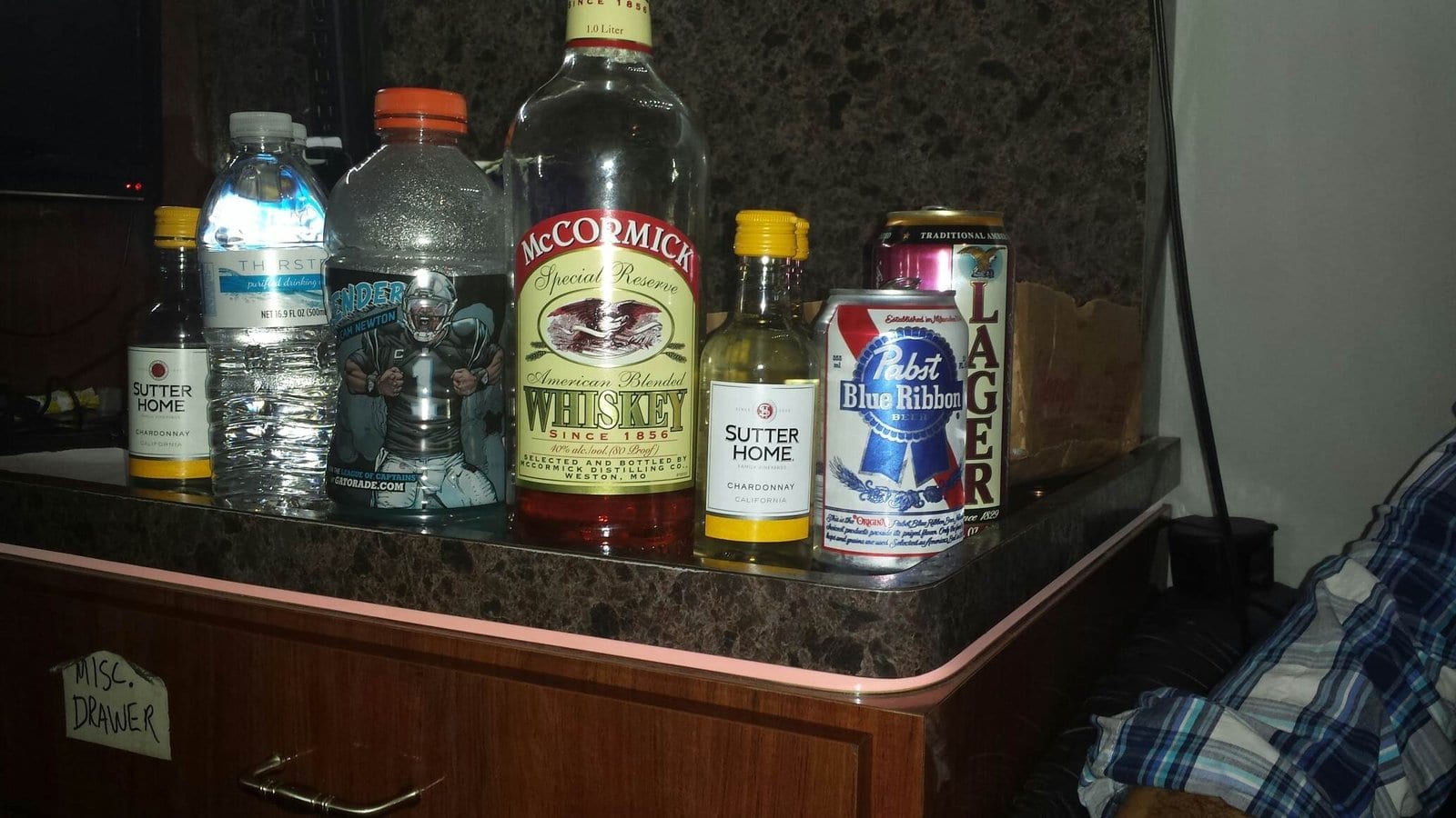 Water, beer, liquor, and mixers sit together on a small wooden cabinet in a compact room.