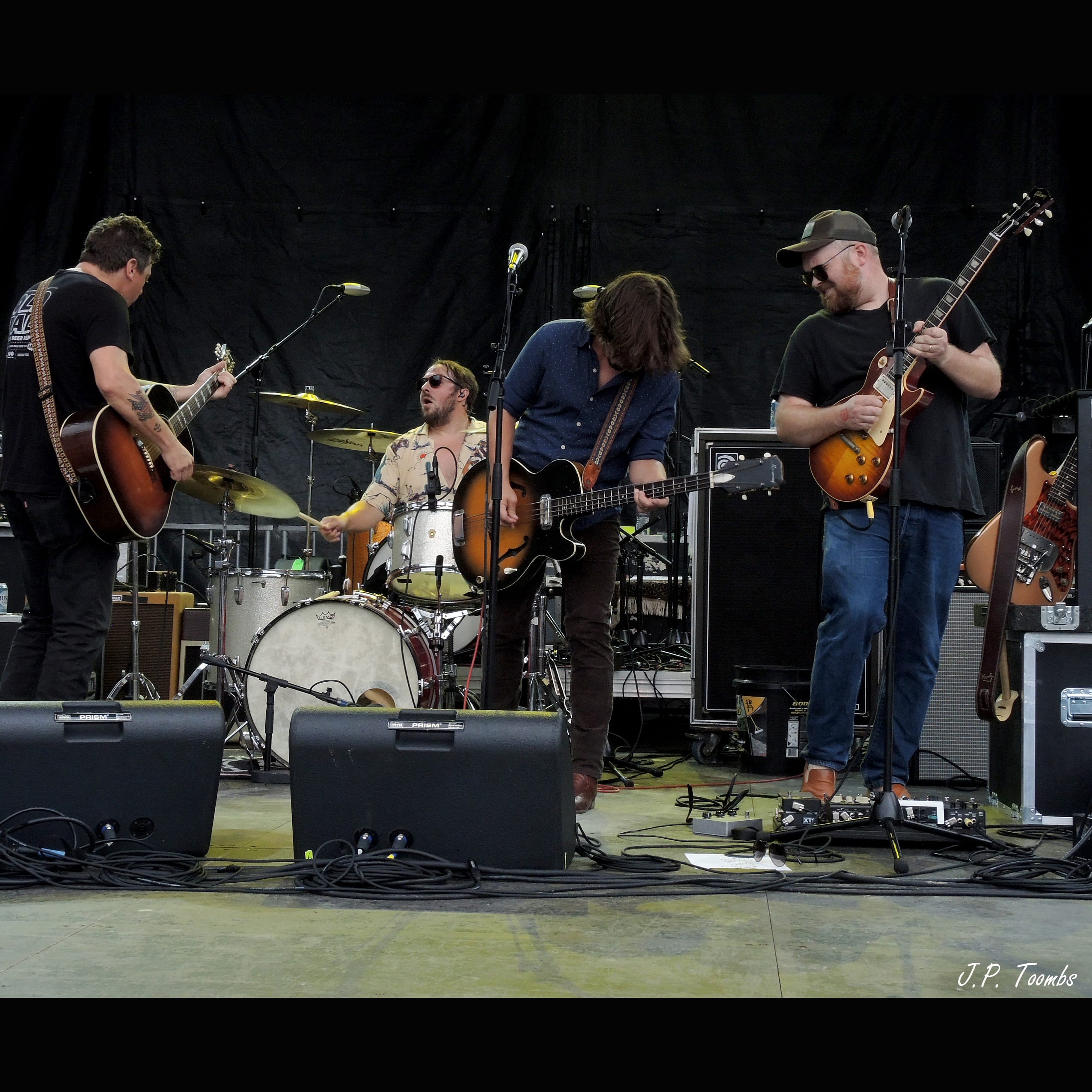 Members of The Wild Feathers gather closely around the drum kit during the outdoor Rock the Ruins performance.