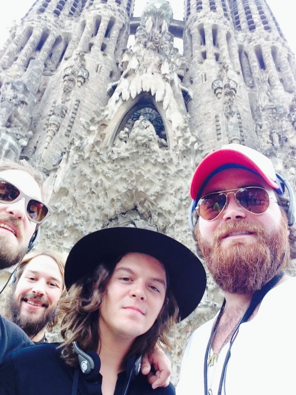 Four unidentified Wild Feathers members taking a close group selfie in front of Barcelona's Sagrada Família.