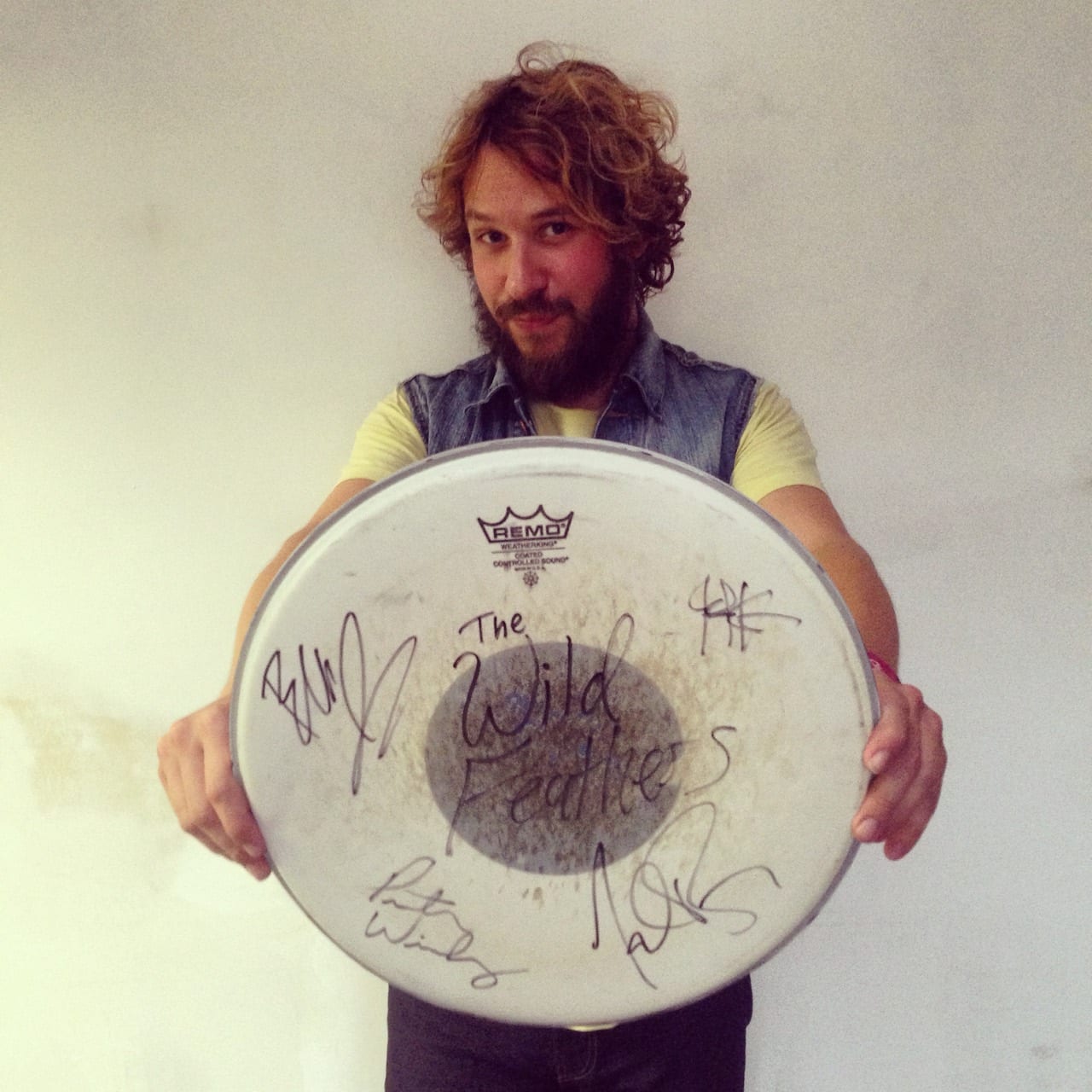 Unidentified band member holding a used drumhead marked The Wild Feathers and covered with signatures.