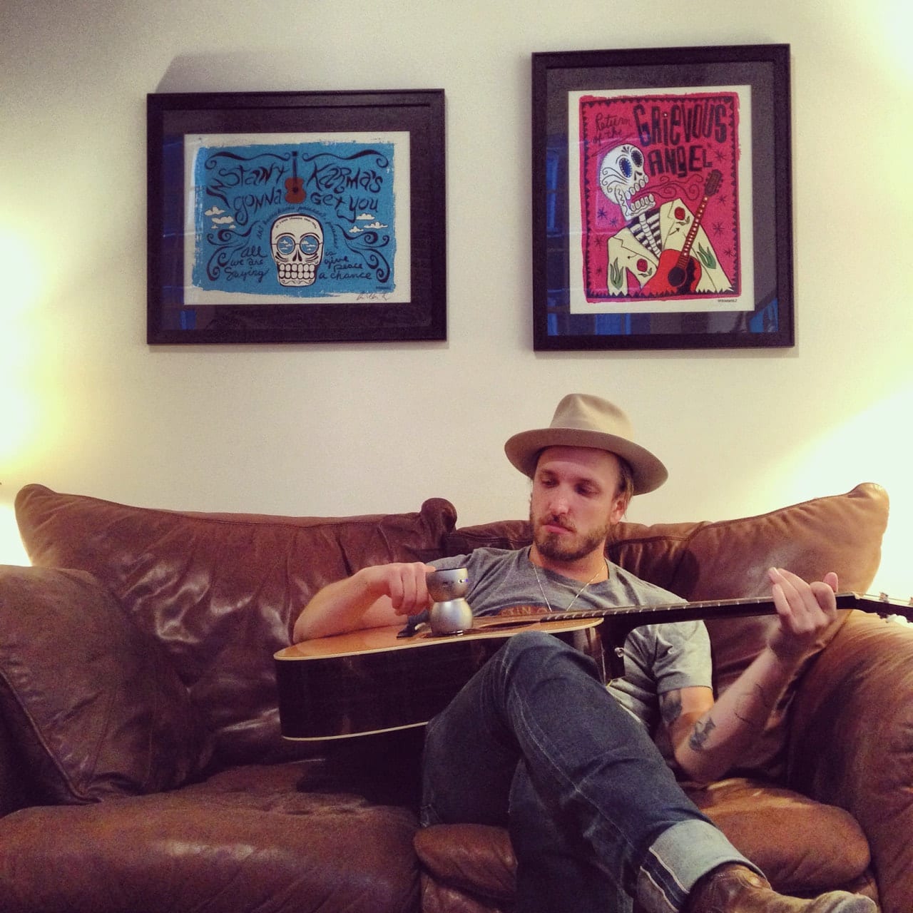 Unidentified Wild Feathers member seated on a couch and playing an acoustic guitar with a metal slide.