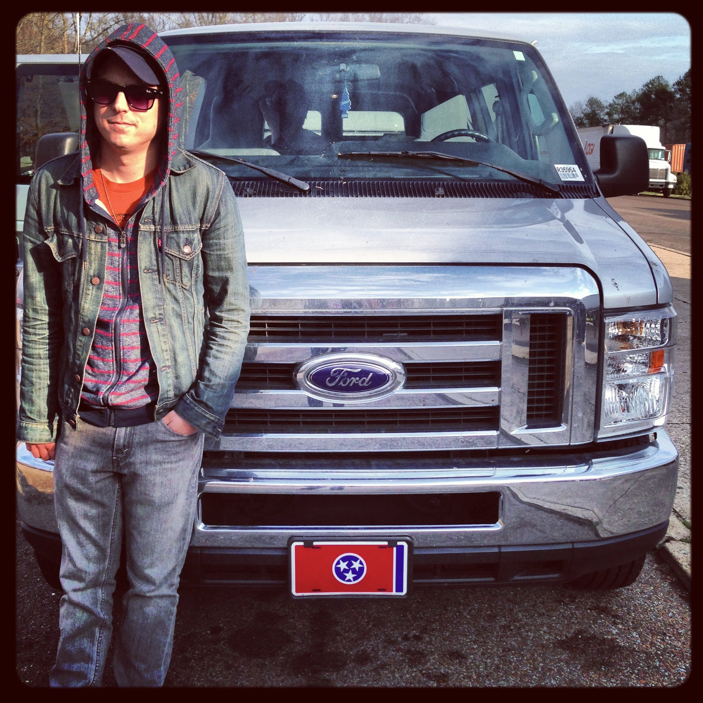 A member of The Wild Feathers standing in front of the touring van at the start of the Southern Residency sequence.