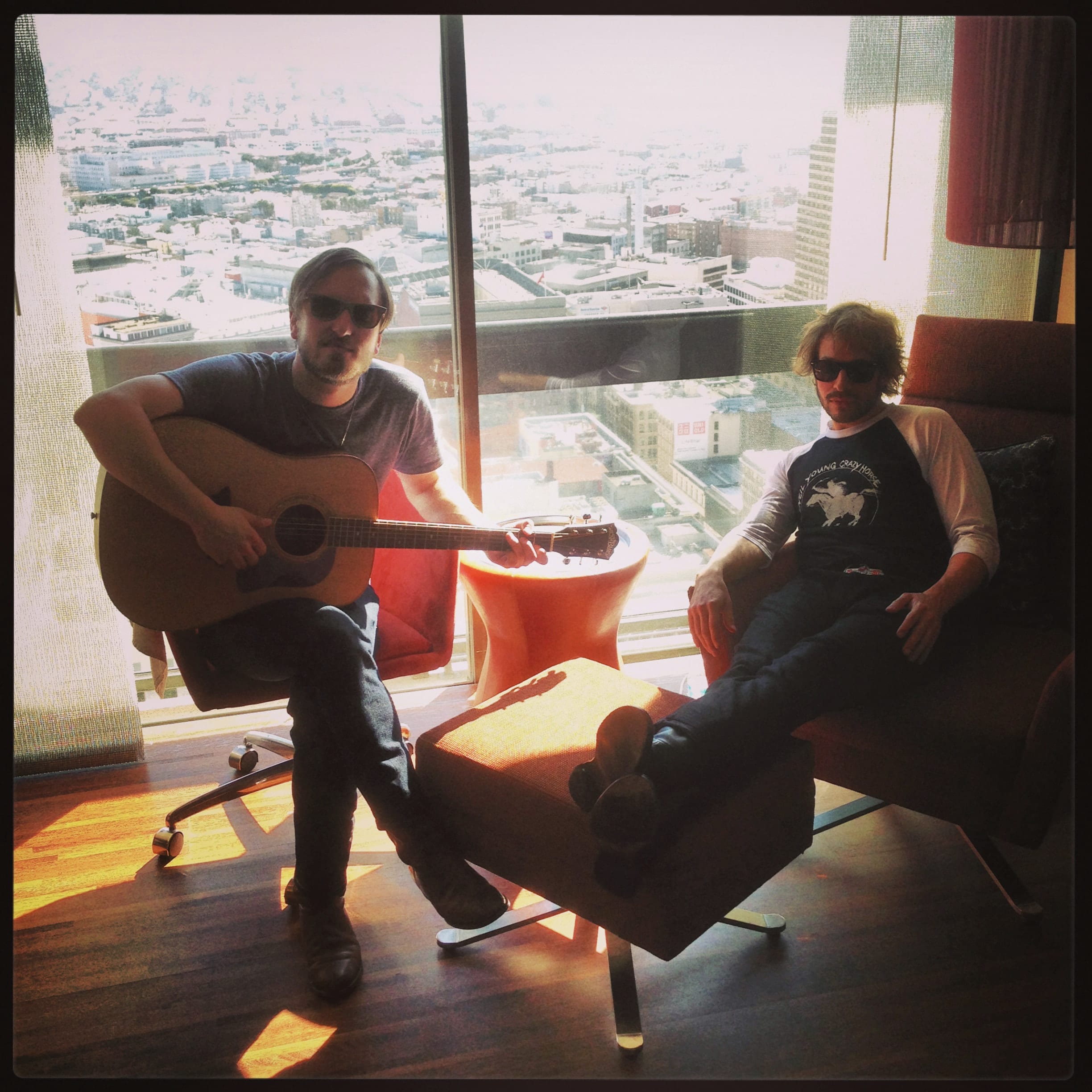 A member of The Wild Feathers playing guitar in a hotel room during the Sunset Sessions sequence.